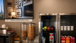 A breakfast bar with cereal dispensers, a refrigerator stocked with fruits and dairy products, and a sign indicating breakfast hours. - Homestead Inn and Suites (Vanderhoof)