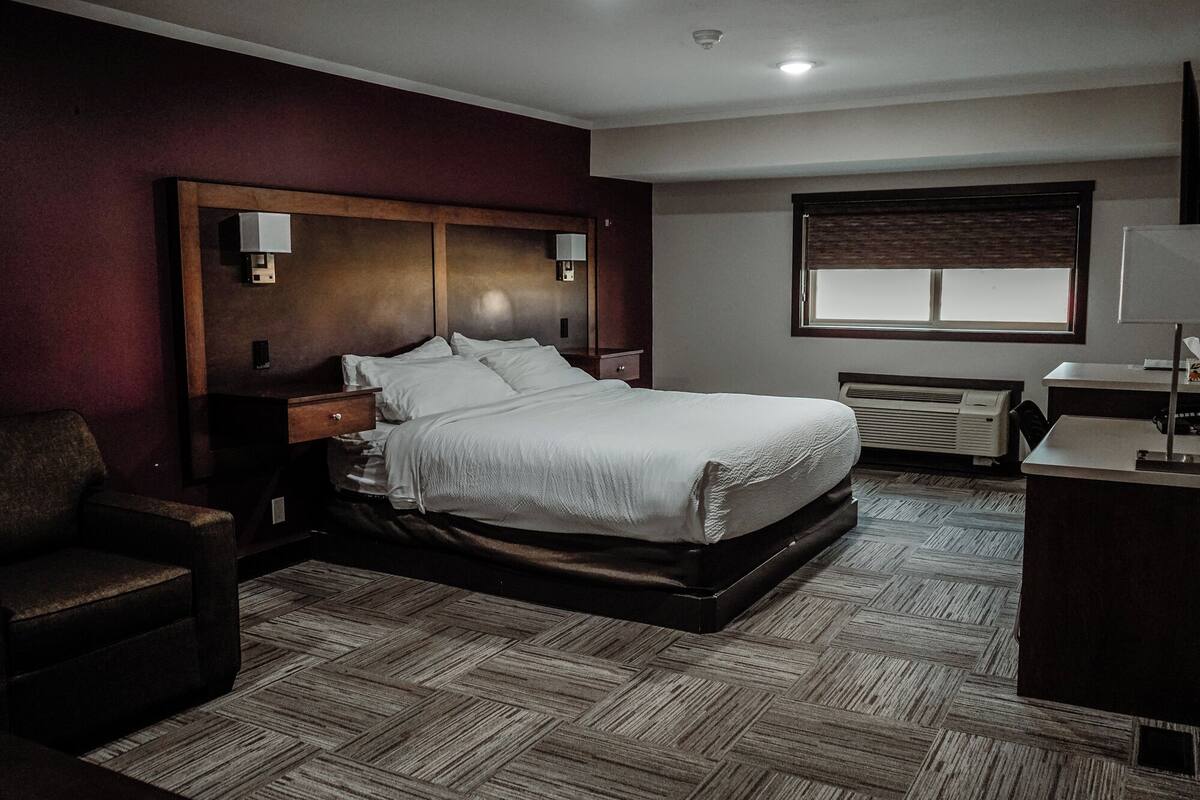 Una habitación de hotel con una cama grande, un escritorio, una silla, una ventana y un calentador fijado a la pared.