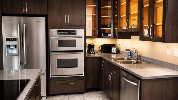 A modern kitchen with stainless steel appliances, dark wood cabinets, and a built-in oven. - Homestead Inn and Suites (Vanderhoof)