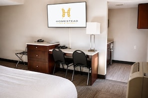 A hotel room with a bed, a desk with a chair, a telephone, a lamp, and a framed sign on the wall. - Homestead Inn and Suites (Vanderhoof)