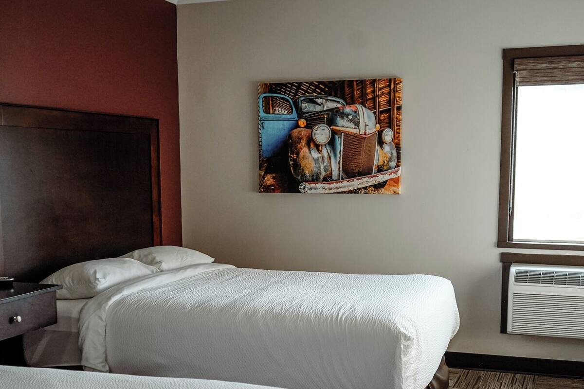 Habitación de hotel con dos camas, cabecero de madera, un cuadro grande y una ventana con persianas.