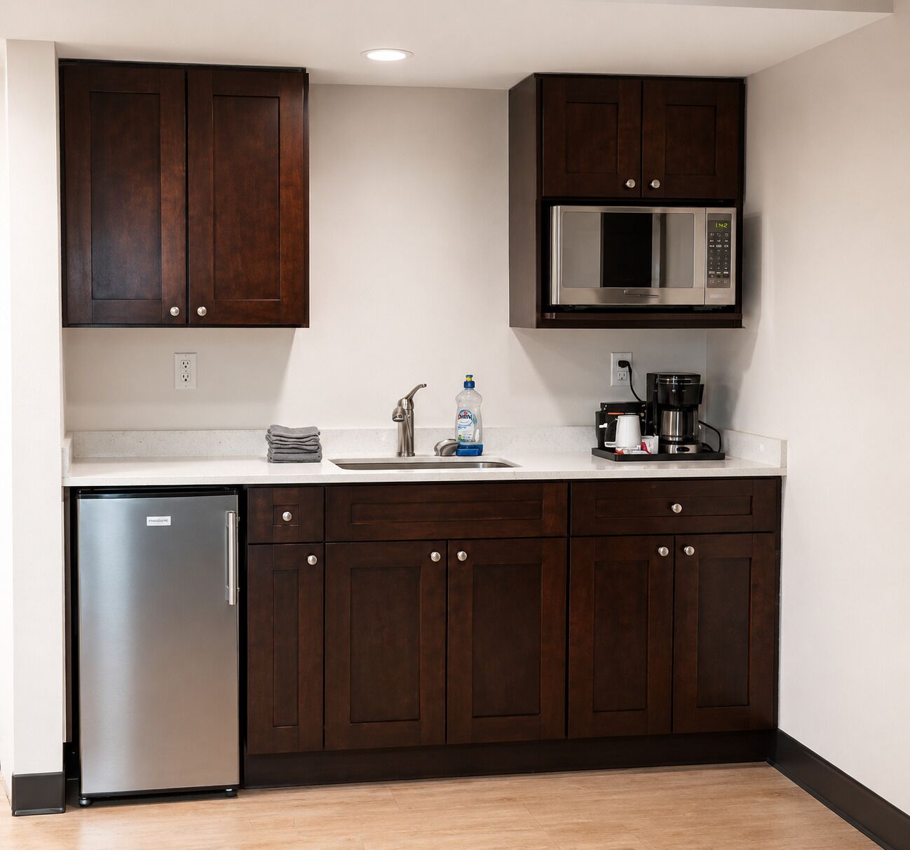 A kitchen with dark wooden cabinets, a stainless steel refrigerator, a microwave, and a coffee maker.