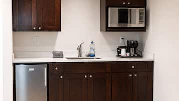 A kitchen with dark wooden cabinets, a stainless steel refrigerator, a microwave, and a coffee maker.