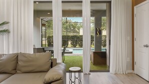 Un salon moderne avec un canapé, une petite table et une porte vitrée donnant sur un espace piscine.