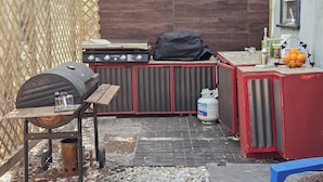 Un área de cocina al aire libre con una parrilla, una estufa de gas portátil y un lavacabezas.