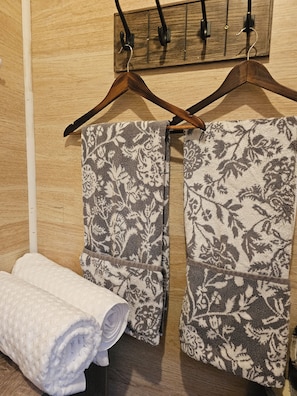 Pared de madera con dos colgadores de madera sujetando toallas estampadas.
