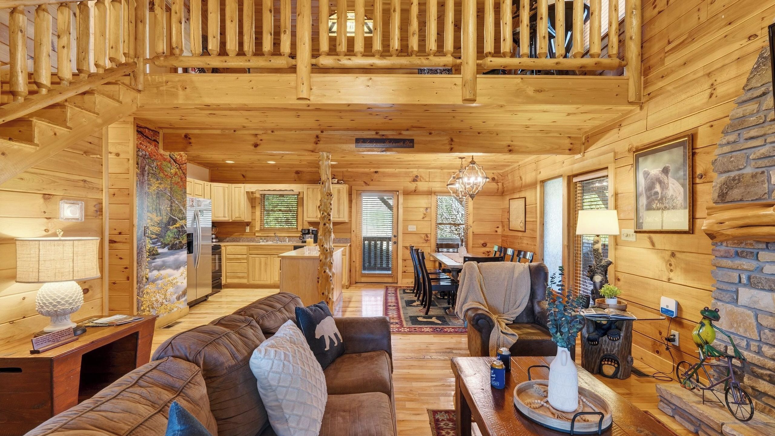 A wooden cabin interior with a dining area, kitchen, and a staircase leading to a loft.