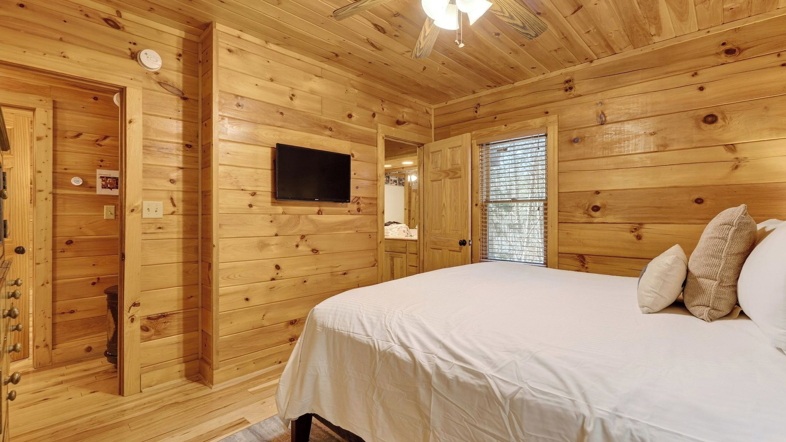 Une chambre dans un chalet en bois, avec un lit, un téléviseur fixé au mur et une fenêtre avec des stores.