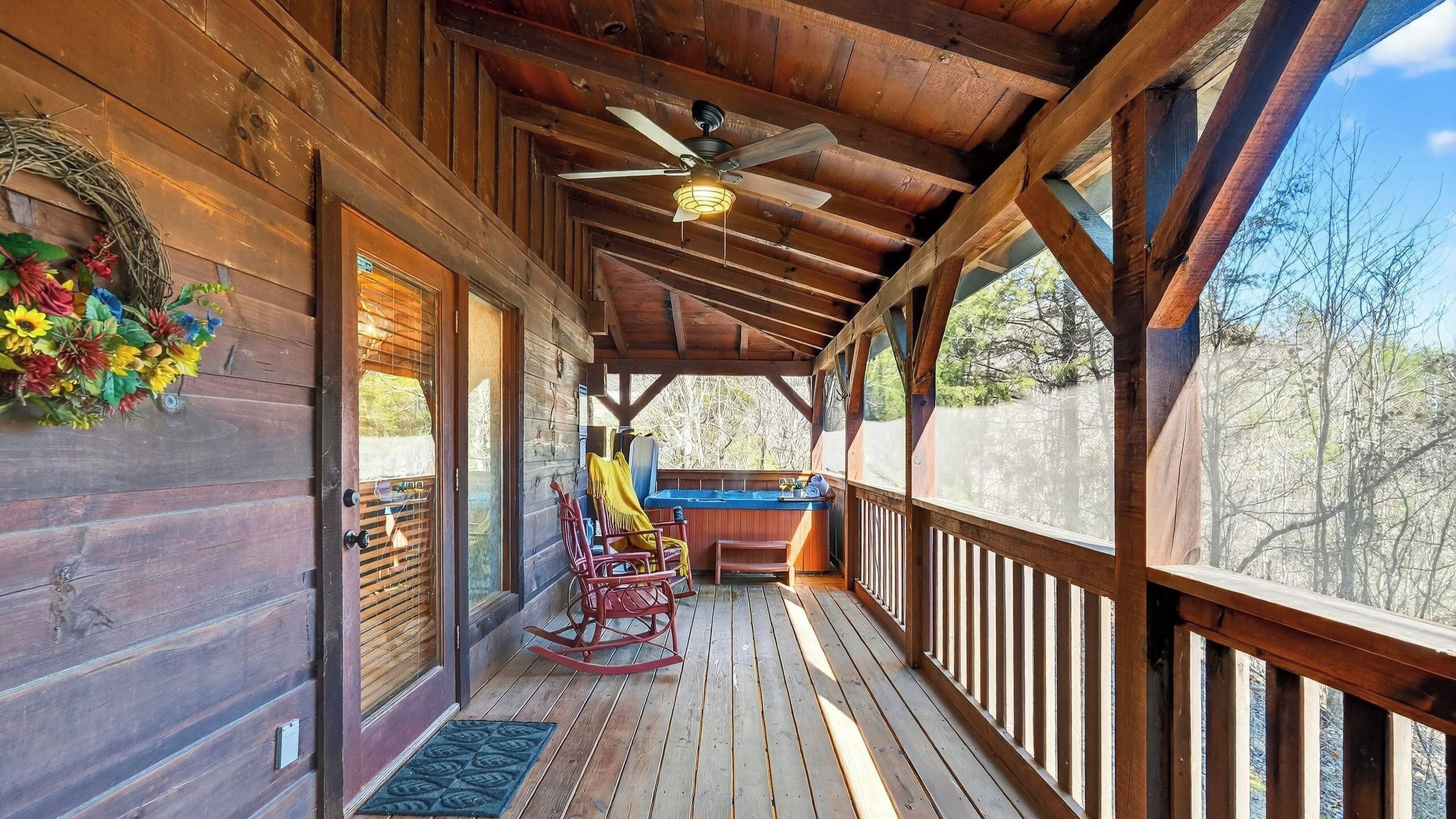 Un portico in legno con una ventola a soffitto, una sedia a dondolo e vista sull'esterno.