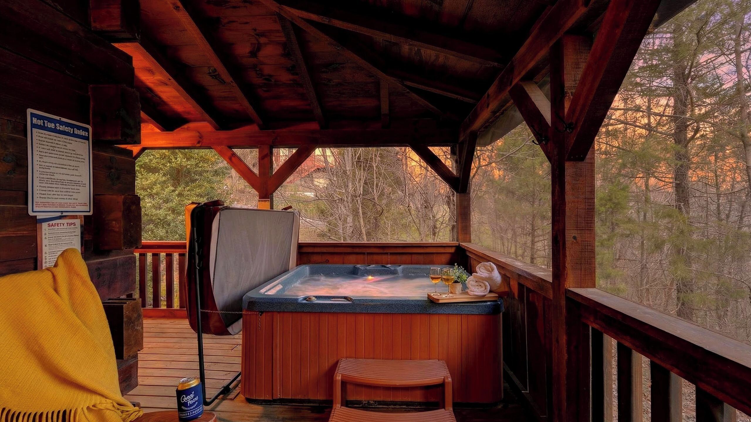 Een houten chalet met een hottub, een stoel en een terras met uitzicht op een bos.