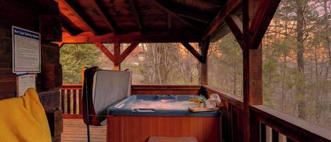 Een houten chalet met een hottub, een stoel en een terras met uitzicht op een bos.