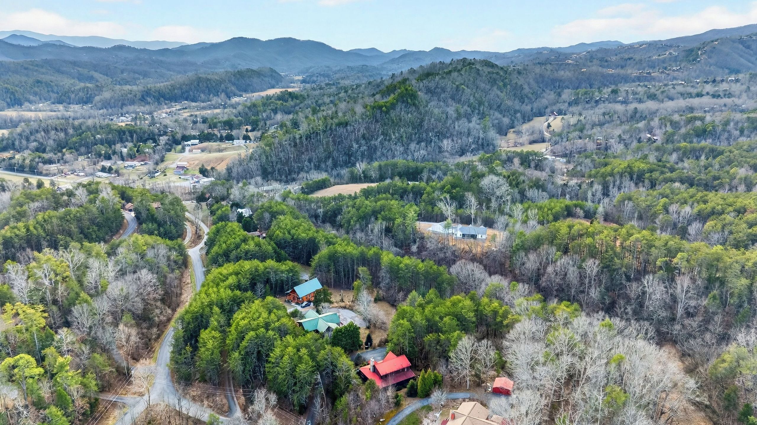 An aerial view of a rural area with scattered houses, dense forests, and a winding road.