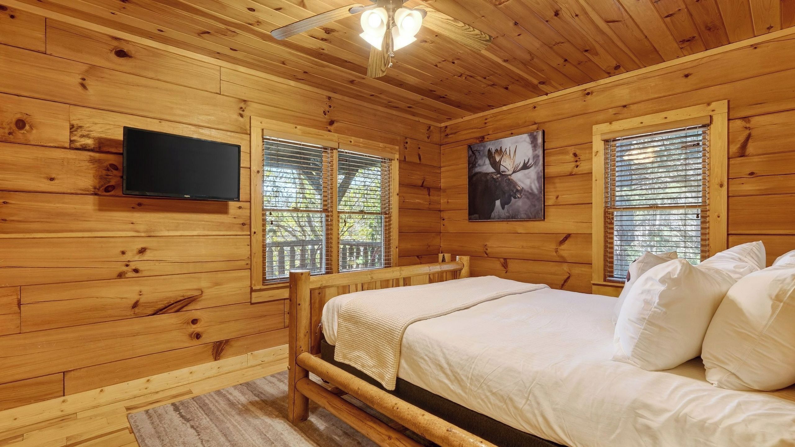 A wooden cabin room with a bed, a television, and windows with blinds.