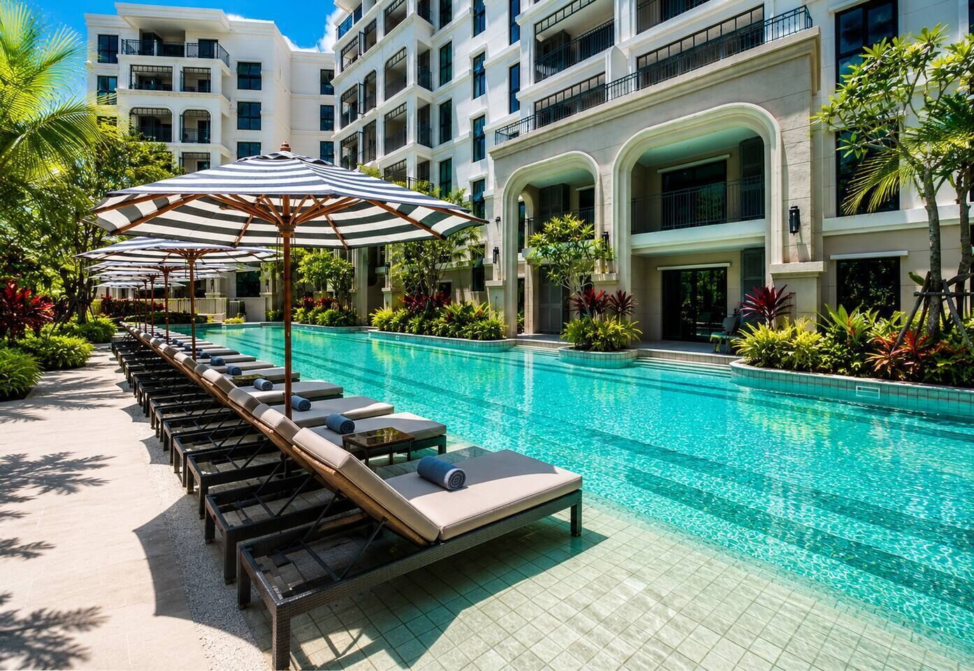 Ein Hotelpoolbereich mit Liegestühlen und Sonnenschirmen, umgeben von einem mehrstöckigen Gebäude mit Balkonen.