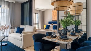 Et moderne hotelværelse med spiseplads, en sofa og en seng med blåt og hvidt sengetøj.
