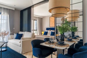 A modern hotel room with a dining area, a sofa, and a bed with blue and white bedding. - Suite Palma 1br the Title Ibg legendary bang tao (Choeng Thale)