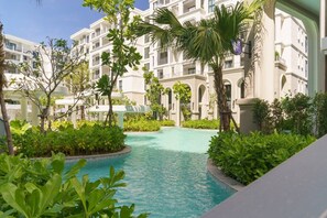 A hotel courtyard with a swimming pool, surrounded by lush greenery and multi-story buildings. - Suite Palma 1br the Title legendary bang tao (Choeng Thale)
