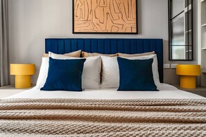 A hotel room with a large bed, two bedside lamps, a blue headboard, and a wall art piece. - Suite Palma 1br the Title legendary bang tao (Choeng Thale)