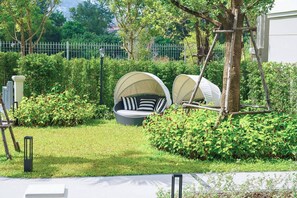 A garden with a seating area featuring two covered chairs and a small table. - Suite Palma 1br the Title legendary bang tao (Choeng Thale)