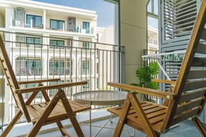 A balcony with wooden chairs and a small table, overlooking a building with multiple balconies. - Suite Valencia 2br the Title Legendary bangtao (Choeng Thale)