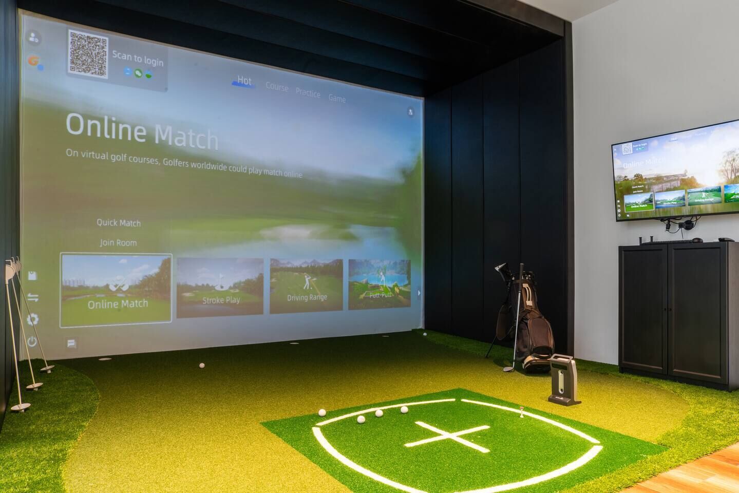 A room with a large screen displaying an online golf match interface, a golf bag, and a television.