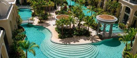 A multi-level hotel with a central swimming pool surrounded by palm trees and a gazebo.