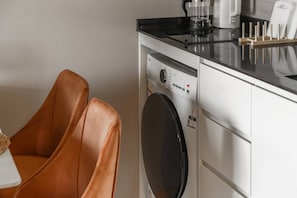 Eine kompakte Küche mit Waschmaschine, Kaffeemaschine und einem Messerblock auf der Arbeitsplatte.