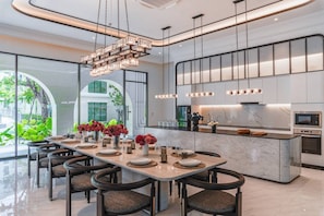 A modern kitchen with a marble countertop, stainless steel appliances, and a dining area with a long table and chairs. - Suite Marbella 1br the Title Legendary bangtao (Choeng Thale)