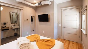 Camera d'albergo con un letto, una televisione, uno specchio, un lavandino e una porta.