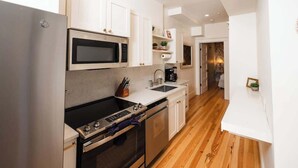 Una cucina moderna con mobili bianchi, un frigorifero in acciaio inossidabile, un forno a microonde, un piano cottura e una lavastoviglie.