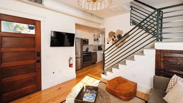 Un soggiorno moderno con una porta in legno, una scala, una TV a schermo piatto e una cucina sullo sfondo.