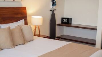 Un lit bien fait, recouvert d’une couvre-lit beige, avec une tête de lit en bois et une étagère fixée au mur, sur laquelle se trouvent une radio et un fer à repasser.