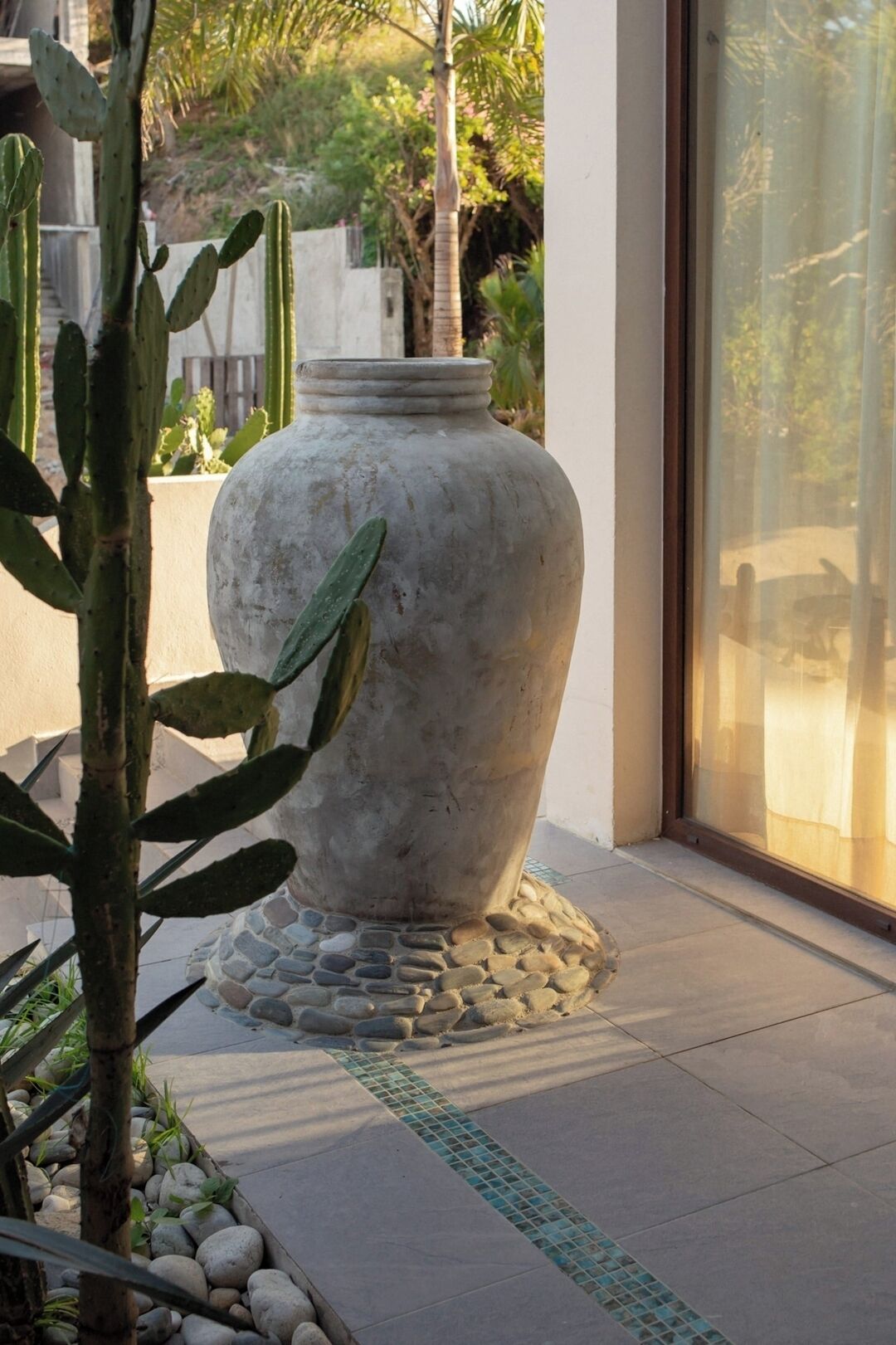 A large stone planter with a cactus plant, placed on a tiled patio with a stone border.