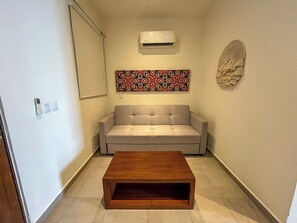 Ein Wohnzimmer mit beiger Couch, Holz-Couchtisch, Klimaanlage und Wandbehang mit Muster.