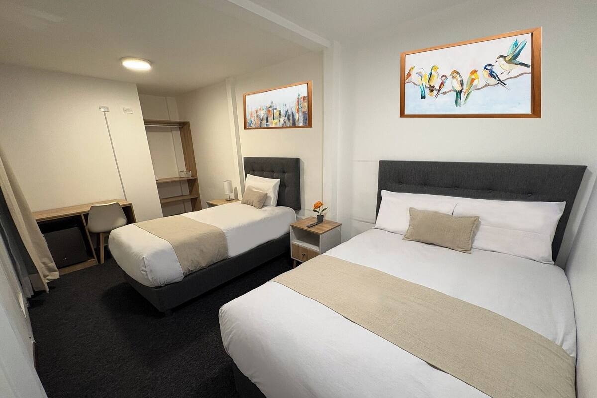 A hotel room with two beds, a desk, a chair, a small table, and artwork on the walls.