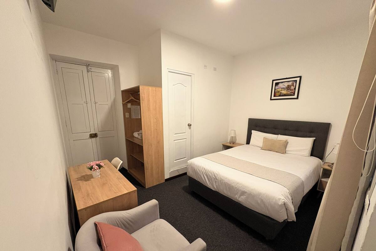 A hotel room with a bed, a desk, a chair, a wardrobe, and a picture on the wall.