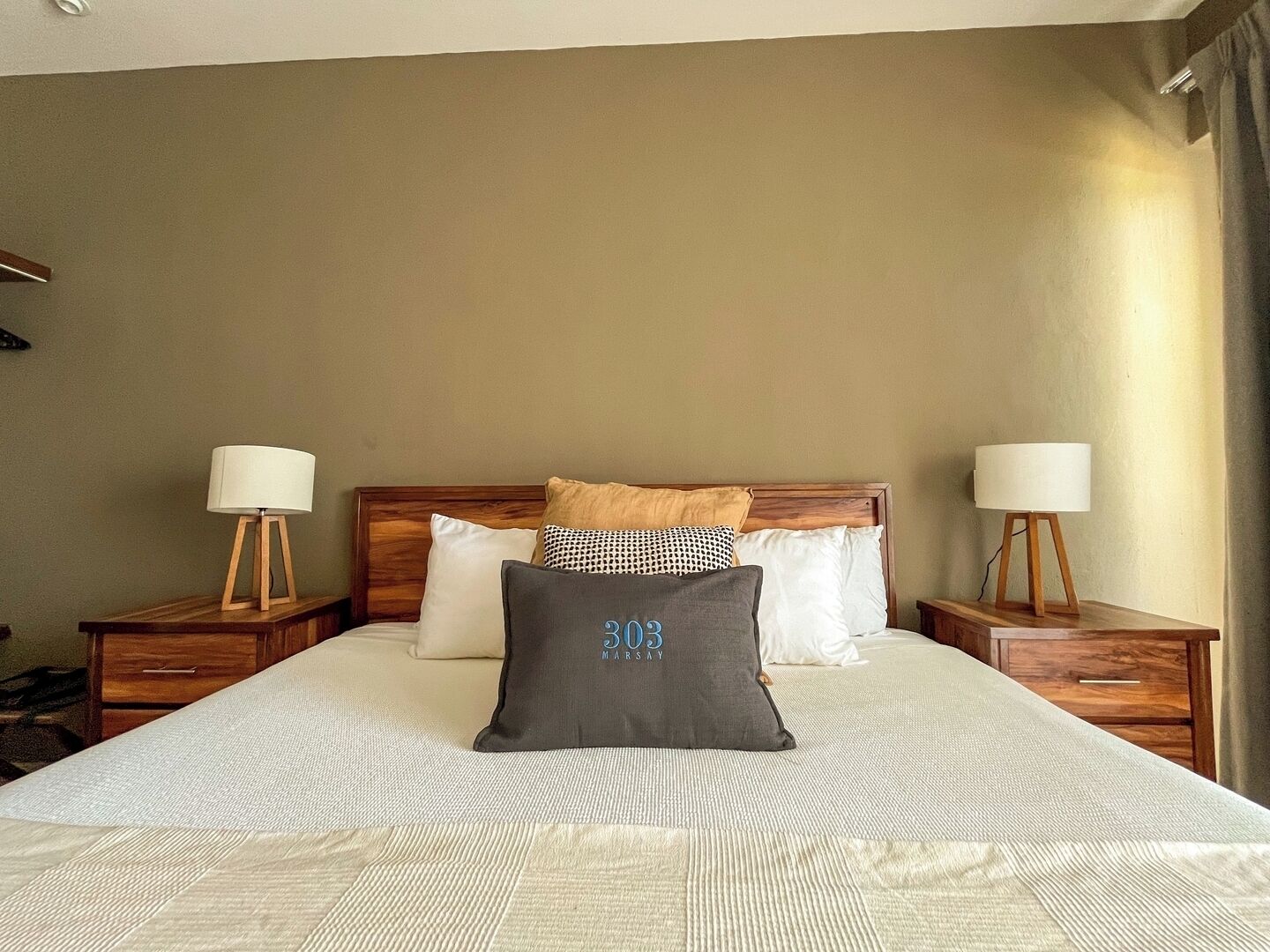Quarto de hotel com uma cama grande, duas mesas de cabeceira com abajures e uma cabeceira com acabamento em madeira.
