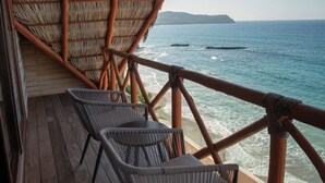 A wooden deck with wicker chairs, a thatched roof, and a view of the ocean.