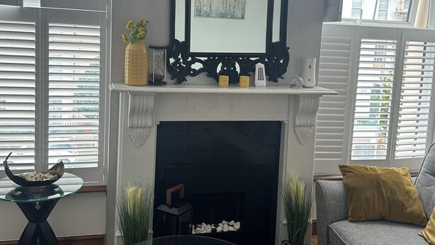 Una sala de estar con chimenea, una mesa redonda de vidrio, un sofá y un espejo decorativo sobre la chimenea.