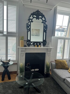 Un salon avec une cheminée, une table basse ronde en verre, un canapé et un miroir décoratif placé au-dessus de la cheminée.