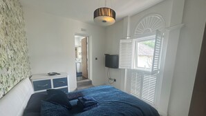 Un dormitorio con cama, mesita de noche, televisor y ventana con contraventanas.
