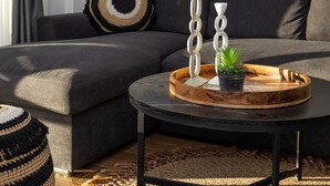 A modern living room with a grey sectional sofa, a round coffee table, and a decorative wall hanging. - Exotic Villa, Private Pool with Lagoon Views – Romantic Escape in Halkidiki (Nea Moudania)
