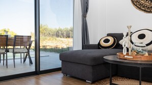 A modern living room with a grey sofa, a round coffee table, and a view of a natural landscape through large windows. - Exotic Villa, Private Pool with Lagoon Views – Romantic Escape in Halkidiki (Nea Moudania)