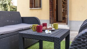 A wicker sofa with cushions, a table with a plate of food and two mugs, and a door leading to a room. - Sweet Dream Apartment 15 min to Venice · Bus 24/7 (Venezia)
