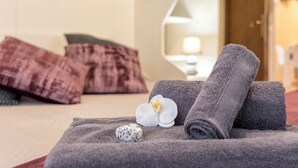A neatly made bed with rolled towels, a white orchid, and a decorative item on a beige bedspread. - Sweet Dream Apartment 15 min to Venice · Bus 24/7 (Venezia)