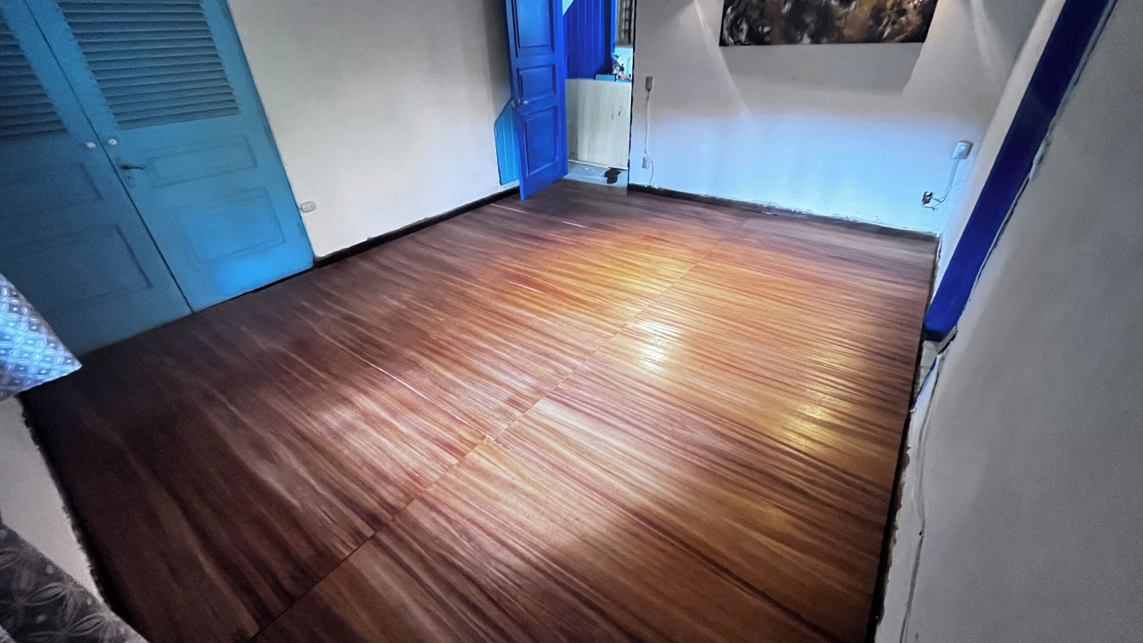 Una stanza con pavimento in legno, una porta blu e una parete bianca con un quadro.