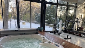 A hot tub with a view of a snowy landscape through large windows.