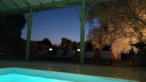 A pool area with lounge chairs, a covered seating area, and a view of trees and rocks.