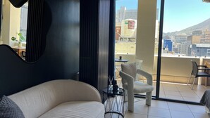 A modern living room with a sofa, a coffee table, and a view of the city through large windows. - Peaceful 1-bedroom apartment in charming Cape Town- The View on Long (Cape Town)