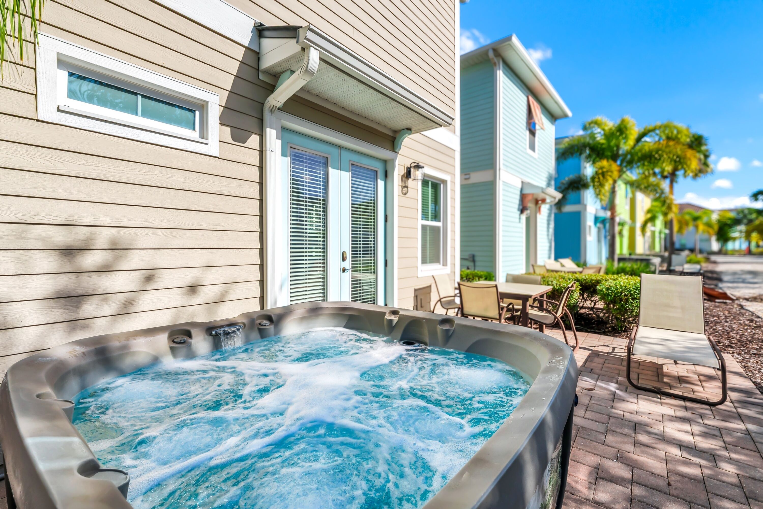 A hot tub in front of a house with a patio and a chair.